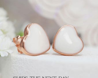 Puede incluir: Un par de pendientes de corazón de oro rosa con esmalte blanco. Los pendientes son pequeños y delicados.