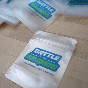 May include: Clear plastic bags with a zip closure, featuring a blue and green logo that reads "BATTLE OF THE BRANDS" and the text "A TRUE 420 CHICAGO LEGACY COMPETITION". Several bags are visible, some overlapping.