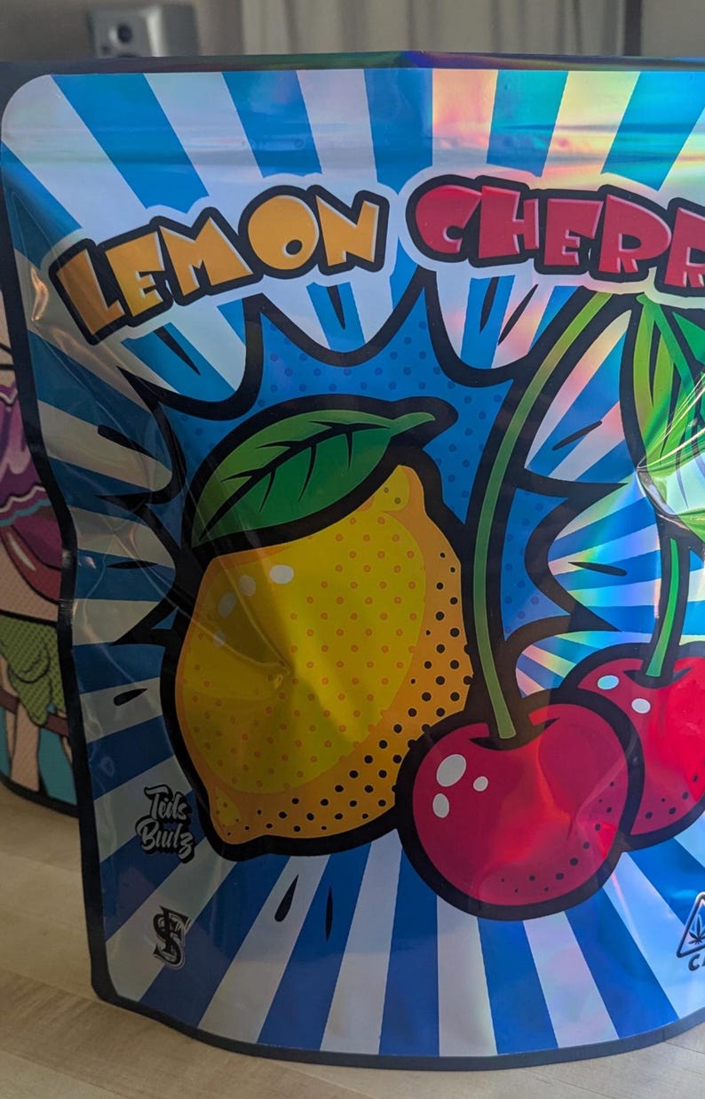May include: A blue and silver package with the words "LEMON CHERRY" in yellow and red. The package features a cartoon illustration of a yellow lemon and two red cherries. The text "Tuts Bulz" is also visible.