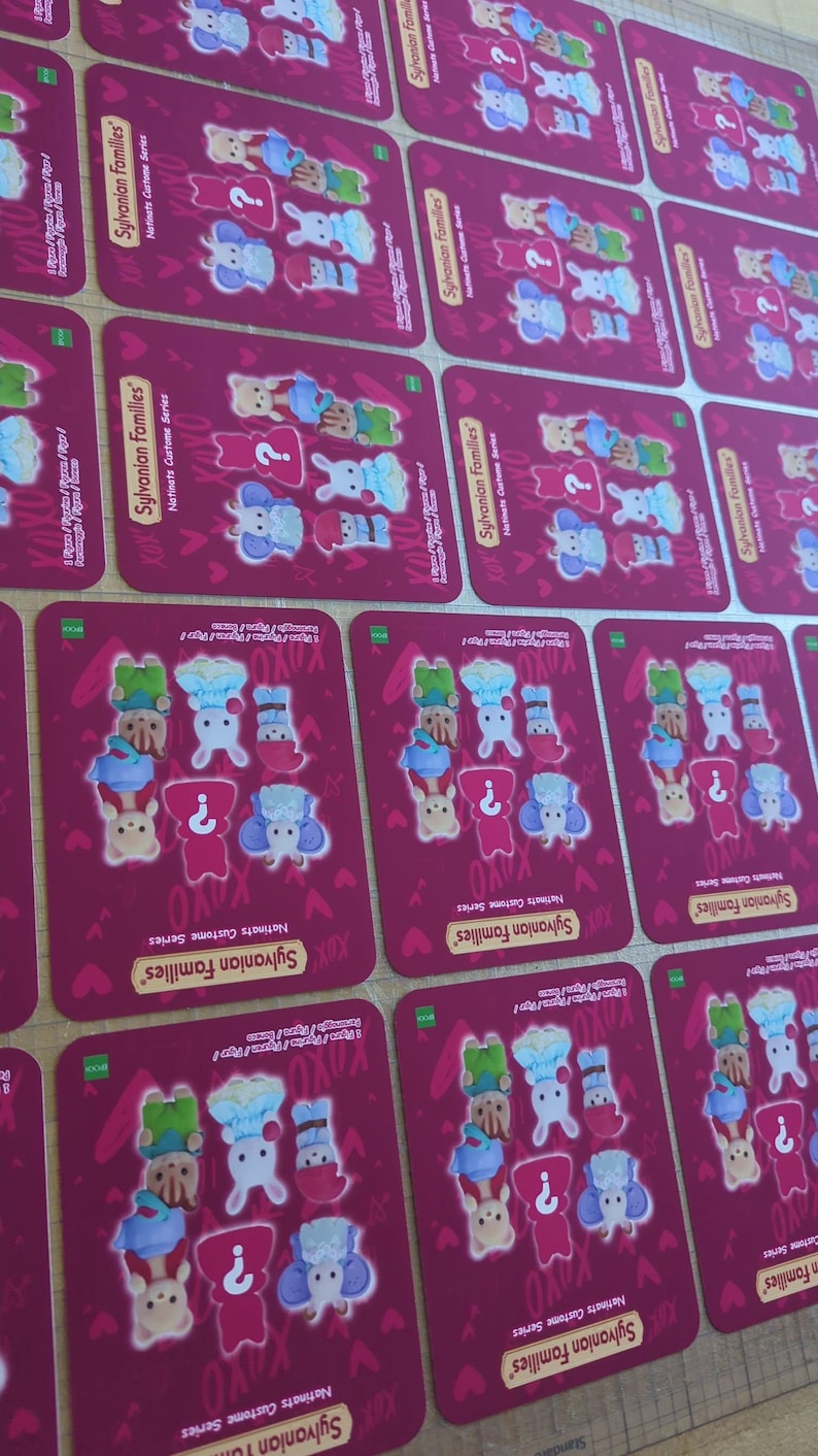 May include: Multiple rectangular cards with a magenta background are arranged on a wooden surface. Each card features illustrations of animal characters in various outfits, with the text "Sylvanian Families" and "Natinats Custome Series".