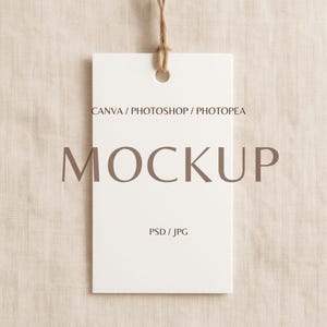 May include: A white rectangular tag with a hole at the top, suspended by a natural twine string. The word "MOCKUP" is printed in a brown font across the tag. The text "CANVA / PHOTOSHOP / PHOTOPAE" and "PSD / JPG" are also visible.