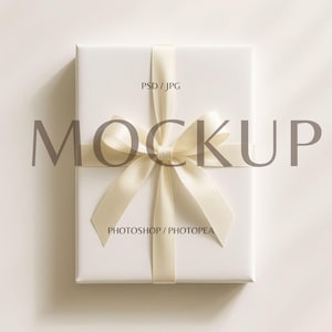 May include: A white gift box tied with a cream-colored satin ribbon and bow. The text "PSD / JPG" is printed on the top right corner, and the word "MOCKUP" is printed in large gray letters across the box. The text "PHOTOSHOP / PHOTOPEA" is printed on the bottom.