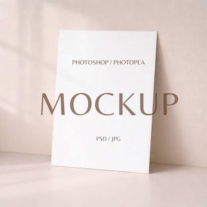 May include: A white rectangular mockup leaning against a light beige wall. The word "MOCKUP" is prominently displayed in large, brown letters. Smaller text above reads "PHOTOSHOP / PHOTOPEA" and below "PSD / JPG".
