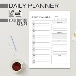 May include: A white daily planner with a minimalist design, featuring a detailed schedule from 6:00 to 23:00, with sections for priorities, reminders, and to-dos. Includes a cup of coffee, pens, and the text "DAILY PLANNER".