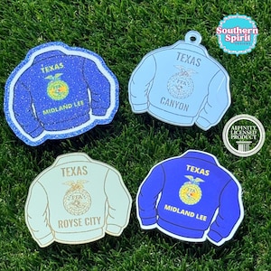 May include: Four jacket-shaped acrylic ornaments featuring FFA emblems. One is blue glitter with 'TEXAS' and 'MIDLAND LEE'. One is light blue with 'TEXAS' and 'CANYON'. One is white with 'TEXAS' and 'ROYSE CITY'. One is blue with 'TEXAS' and 'MIDLAND LEE'.