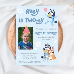 May include: A light blue birthday invitation card featuring cartoon dog characters, white daisy graphics, and a photo of a child wearing a pink party hat. The text reads Ruby is two-ey, Ruby's 2nd Birthday, Saturday, October 10th at 2:00pm, and address details.