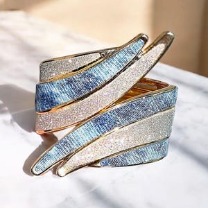 Puede incluir: Un brazalete de denim azul y dorado con un acabado brillante. El brazalete está hecho de múltiples capas de denim y metal dorado.