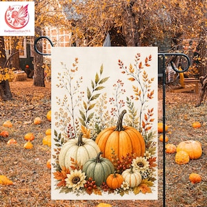 Pode incluir: Uma bandeira de jardim retangular com uma ilustração impressa de três abóboras em laranja, branco e verde, rodeadas por girassóis, folhas de outono e ervas altas secas num fundo creme, pendurada num suporte de metal preto.