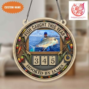 Puede incluir: Decoración de pared de madera con temática de pesca con una foto de una persona sosteniendo un pez grande. Se muestra el texto "FISH CAUGHT THIS YEAR" y "HOOKED BY JAMES". El contador muestra "345". Incluye señuelos de pesca y el texto "CUSTOM NAME".