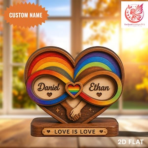 Puede incluir: Decoración de madera en forma de corazón con detalles de arcoíris y la frase "Love is Love". El diseño presenta dos símbolos de infinito, los nombres "Daniel" y "Ethan" y un corazón de arcoíris. También se ve el texto "Custom Name".