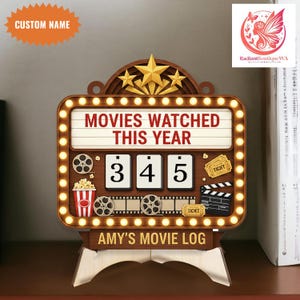 Puede incluir: Registro de películas de madera con el texto "MOVIES WATCHED THIS YEAR" y "AMY'S MOVIE LOG". El registro tiene un diseño de marquesina con luces, estrellas e iconos de carretes de película. El contador muestra "345".