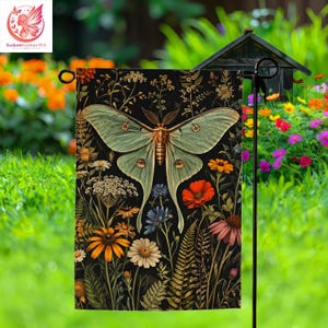 May include: A garden flag featuring a large, light green moth with intricate wing patterns, set against a black background filled with colorful flowers and foliage. The flag is displayed outdoors in a garden setting.