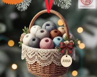 May include: A Christmas ornament shaped like a woven basket filled with colorful yarn balls. The basket has a lace trim and a red ribbon for hanging. A tag with the name "ANNA" hangs from the basket. The words "CUSTOM NAME" and "2D FLAT ITEM" are also visible.