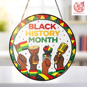 May include: Round glass Black History Month hanging decoration. The design features the text "Black History Month" with illustrations of a flag, drum, comb, fist, and microphone, all in the colors of the Pan-African flag. The decoration is framed with a colorful border and hangs from a chain.