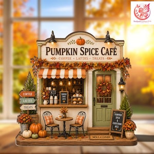 Op de afbeelding: Een miniatuurmodel van een Pumpkin Spice Café met een winkelpui met gestreepte luifel, een groene deur en herfstbladeren. Het bord leest PUMPKIN SPICE CAFÉ, COFFEE, LATTES, TREATS. Inclusief een klein tafeltje, twee stoelen, pompoenen en een welkomstmat.