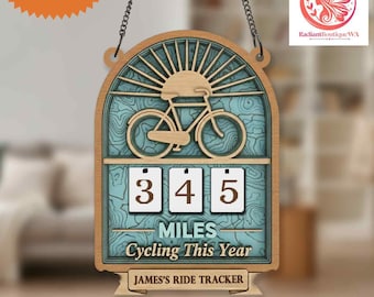May include: Wooden cycling tracker with a bicycle silhouette, sunburst design, and the text "345 MILES Cycling This Year." Includes a chain for hanging and the text "JAMES'S RIDE TRACKER." Features a custom name tag.