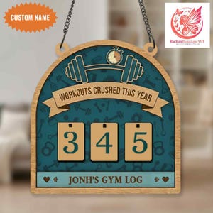 Puede incluir: Letrero de registro de gimnasio de madera con fondo verde azulado y marco de madera clara. El letrero presenta el texto "WORKOUTS CRUSHED THIS YEAR" y un contador que muestra "345". Incluye el texto "JONH'S GYM LOG" y una etiqueta de nombre personalizada.