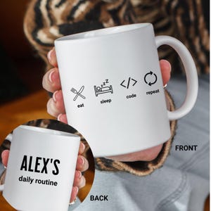 Puede incluir: Taza de cerámica blanca con las palabras "eat, sleep, code, repeat" e iconos relacionados. La parte posterior de la taza dice "ALEX'S daily routine" en texto negro. La taza tiene un asa grande.