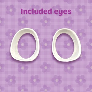 May include: Two white, oval-shaped eye molds are shown against a purple floral background. The text "Included eyes" is written in a purple font above the molds. The background has a checkered pattern with flower designs.