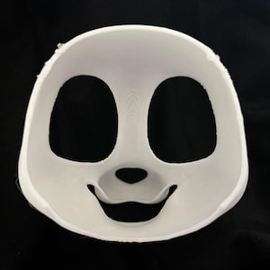 May include: A white, 3D-printed mask with large oval eye holes and a smiling mouth. The mask has a smooth surface and is designed to fit the face. The background is black.