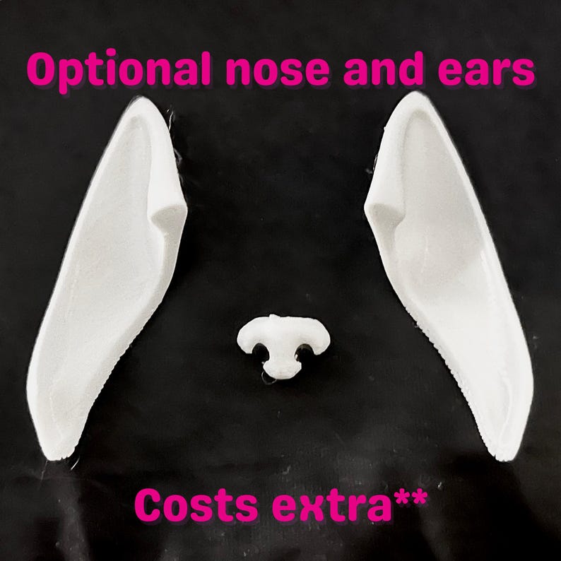 May include: White plastic bunny ears and nose on a black background. The text "Optional nose and ears" is above the ears, and "Costs extra**" is below. The ears are long and pointed, and the nose is small and rounded.