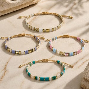 Peut inclure: Quatre bracelets réglables composés de petites perles carrées aux couleurs variées, notamment blanc, doré, violet, rose, bleu et turquoise. Chaque bracelet est doté d'un fermoir à nœud coulissant en cordon beige fin pour un ajustement personnalisé.