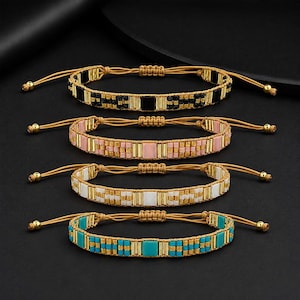 Puede incluir: Cuatro pulseras de cuentas en negro, rosa, blanco y turquesa. Cada pulsera presenta un diseño tejido con detalles dorados y cierres de cordón ajustables. Las pulseras se exhiben sobre una superficie oscura.