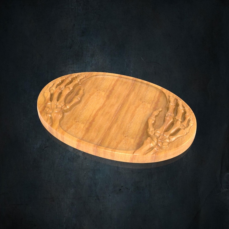 K&ouml;nnte beinhalten: Ein ovales Serviertablett aus Holz mit einer nat&uuml;rlichen hellbraunen Holzmaserung. Das Tablett ist mit zwei detaillierten Skeletthand-Motiven geschnitzt, eines auf jeder Seite, die sich zur glatten, vertieften Mitte der Oberfl&auml;che hin erstrecken.