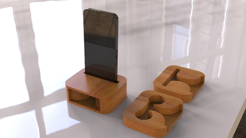 May include: A wooden phone stand with a slot to hold a phone upright. Two wooden coasters with the letters "A" and "B" are also present. The items are made of light brown wood and sit on a white surface.