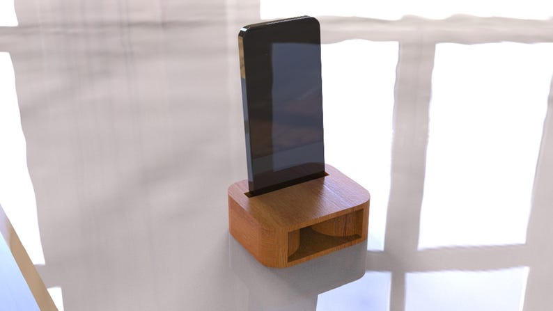 May include: A wooden phone stand with a slot to hold a smartphone upright. The stand is made of light brown wood and has a rectangular base with a curved top. The phone is black and has a rectangular shape.