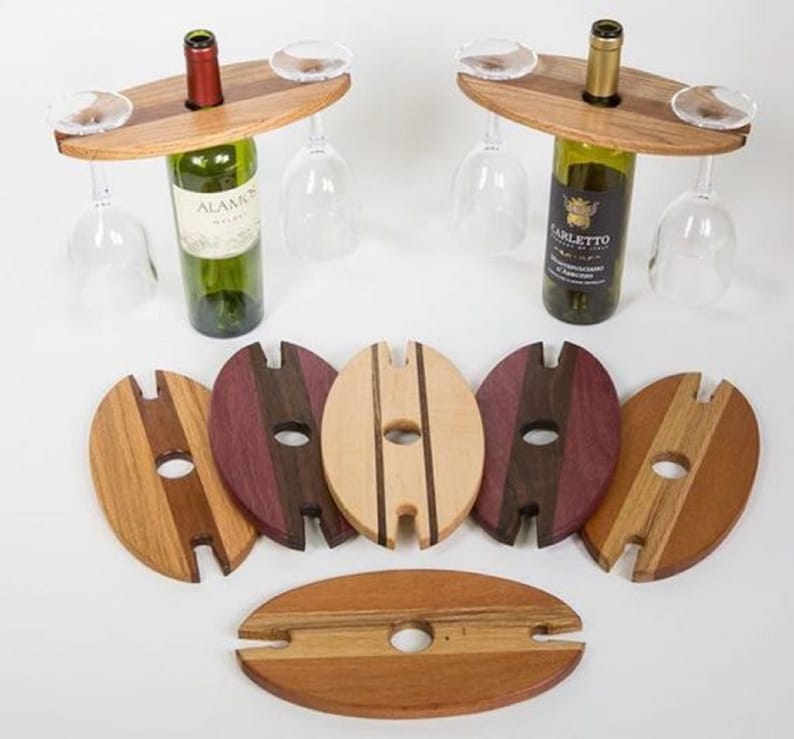 May include: Wooden wine bottle and glass holders with a natural finish. The holders have a circular hole for the bottle and slots for wine glasses. Several wooden coasters in various wood tones are also included.
