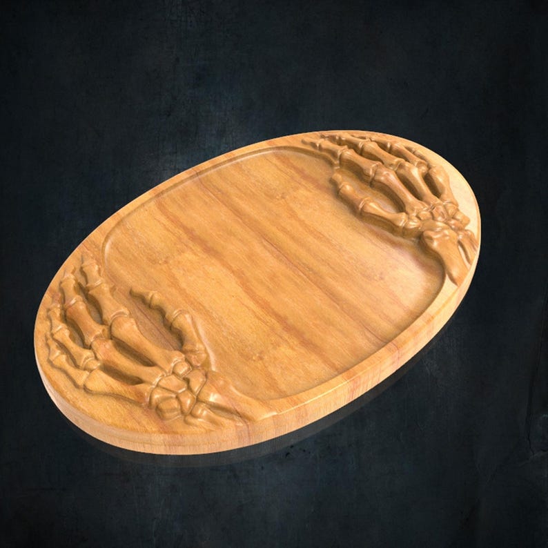 K&ouml;nnte beinhalten: Ein ovales Serviertablett aus Holz mit zwei geschnitzten Skeletth&auml;nden, die aus den Seiten hervorragen. Die hellbraune Holzmaserung ist auf der glatten, vertieften Mittelfl&auml;che sichtbar, w&auml;hrend die Knochenstrukturen erhaben sind.