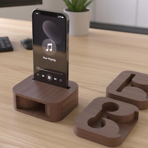 May include: A wooden phone stand with a phone displaying a music app. Two matching wooden coasters are next to the stand. The stand and coasters are made of dark brown wood and sit on a light brown wooden desk.