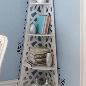 May include: White corner shelf unit with 4 shelves. The shelf is 25 inches wide, 28 inches tall, and 90 inches high. The shelves have a decorative cut-out design and are perfect for displaying books, plants, and decorative items.