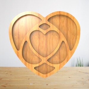 May include: A wooden heart-shaped tray with a nested heart design. The tray is made of light-coloured wood and features a cutout design. The tray is sitting on a wooden surface.
