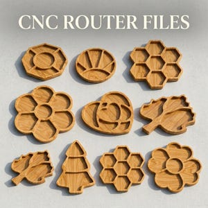 May include: A collection of wooden serving trays in various shapes, including a flower, heart, leaf, and honeycomb design. The text "CNC ROUTER FILES" is displayed at the top. The trays are made of light-colored wood.