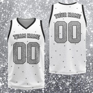 May include: White athletic jersey with black trim and a V-neck. The front displays "TEAM NAME" above the number "00" in silver glitter. The back shows "YOUR NAME" above the number "00". Small black stars are scattered across the jersey.