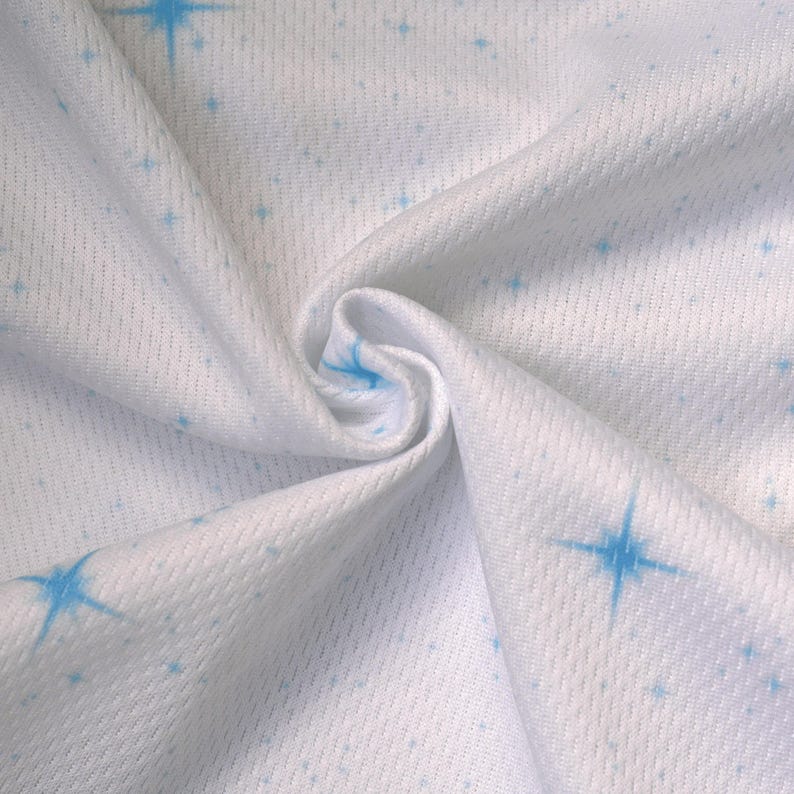 May include: White fabric with a subtle texture, adorned with a pattern of small and large blue starbursts. The fabric is gathered, creating soft folds and shadows, highlighting the star design. The material appears to be lightweight.