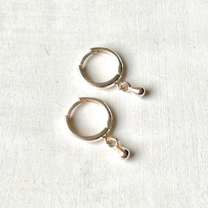 May include: A pair of silver hoop earrings with a small silver ball dangling from each hoop.
