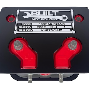 May include: Black battery box with red terminals and a white sticker that reads "BUILT NOT BOUGHT" with the details "MODEL 1965 MUSTANG BUILT IN 2022 NO 1 BUILT BY KURT WILLIS"
