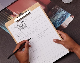 May include: A daily mind and body journal with a checklist for tracking sleep, water intake, movement, and gratitude. The journal is on a clipboard with a wooden frame.