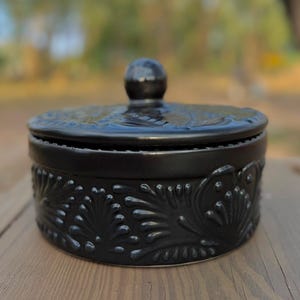 May include: Black ceramic trinket box with a lid. The box has a floral design embossed on the sides.
