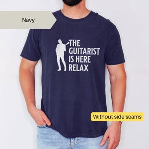 May include: A navy blue t-shirt with the text "The Guitarist is Here Relax" in white. The shirt features a silhouette of a person playing a guitar. The text "Without side seams" is visible in a yellow box.