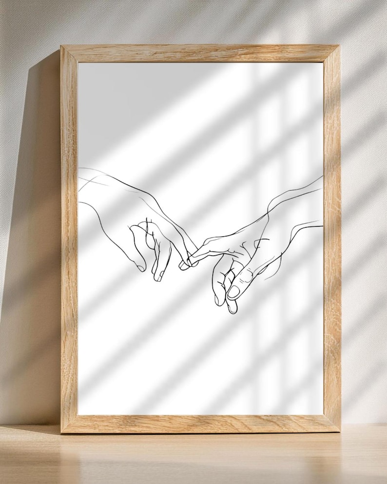 May include: A black and white line drawing of two hands reaching towards each other, with fingers intertwined. The drawing is framed in a light wood frame.