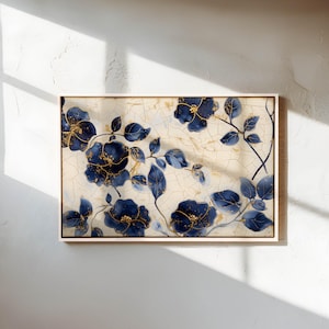 May include: A framed floral art print featuring navy blue flowers with gold accents and green leaves against a cream-colored background. The artwork is in a light-colored wooden frame, creating a sophisticated and elegant aesthetic.
