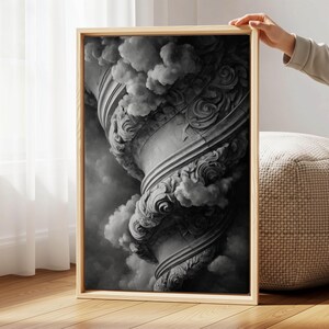 Op de afbeelding: Zwart-wit ingelijste kunstdruk met een gedetailleerde afbeelding van een klassiek architecturaal element, mogelijk een zuil of vaas, met wervelende versieringen en wolkvormige vormen. Het kunstwerk wordt door een persoon vastgehouden.
