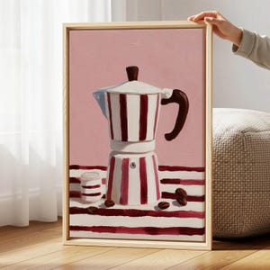 Peut inclure: Peinture encadrée d'une cafetière à rayures rouges et blanches, d'une petite tasse et de grains de café sur une surface rayée. Le fond est rose uni. La cafetière a une poignée et un dessus marron.