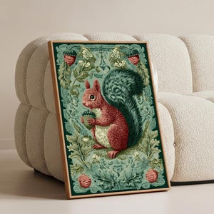 Puede incluir: Una impresión artística enmarcada que presenta una ardilla roja sosteniendo una bellota. La ardilla tiene una cola tupida verde y negra. El fondo es un patrón floral verde y azul verdoso con bayas rojas. El marco es de color marrón claro.