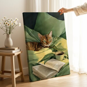 May include: A canvas print featuring a watercolor painting of a Bengal cat with green eyes, resting on a green blanket. A cup of coffee and an open book are also depicted. A vase of white flowers sits on a wooden stool.