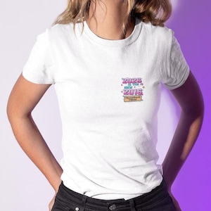 Puede incluir: Camiseta blanca con un pequeño gráfico colorido en el pecho. El gráfico dice "2026 is the new 2016" con "Throwback Vibes!" debajo. La camiseta tiene mangas cortas y cuello redondo.